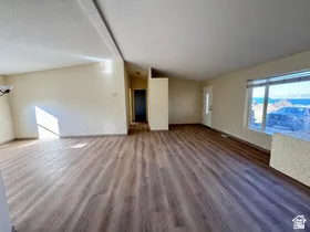 Spacious room featuring wood-finish flooring, vaulted ceilings, and a large window