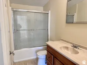 Bathroom featuring a wood-finish vanity with an integrated sink, a mirrored medicine cabinet, a toilet, and a bathtub with sliding glass doors