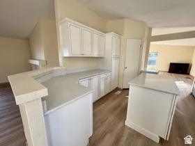 Updated kitchen featuring white cabinetry, light-toned countertops, a central island, a breakfast bar, and wood-finish flooring