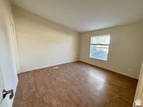Vaulted ceiling, wood-finish flooring, and a window with blinds