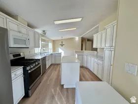 Kitchen featuring wood-finish flooring, white cabinetry, a central island, stainless steel appliances, and ample counter space