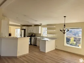 Kitchen with white cabinetry, stainless steel appliances, wood-finish flooring, and a dining area with chandelier lighting