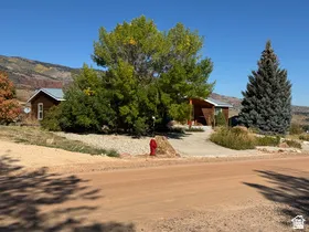 Wood-sided exterior with a metal roof, mature trees, and a gravel driveway