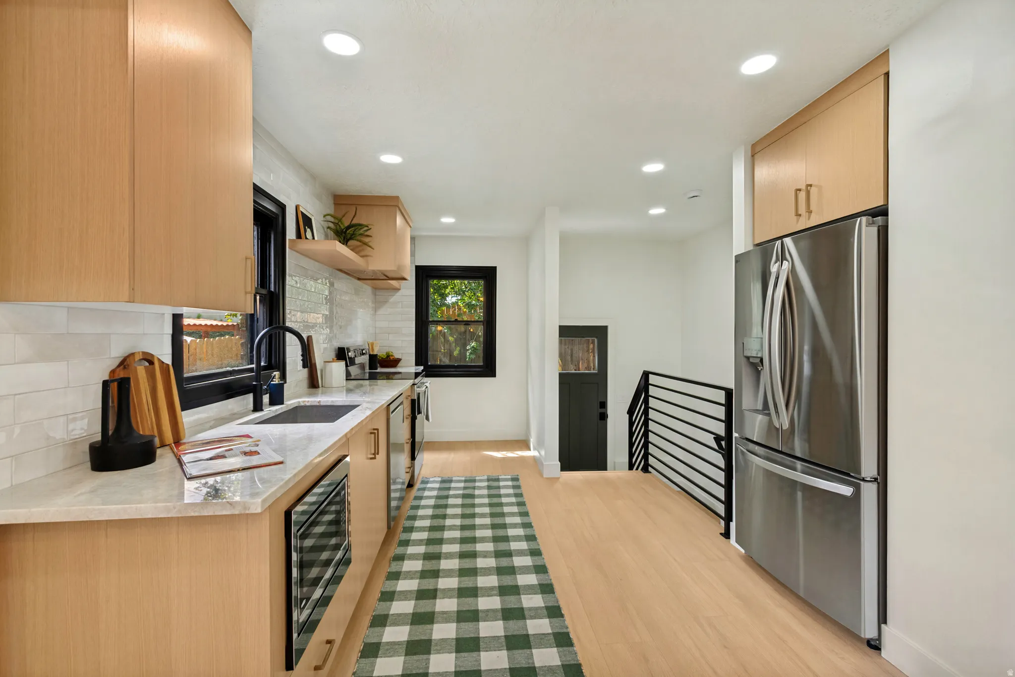 Kitchen featuring light wood-finish cabinetry, light stone countertops, a tile backsplash, and stainless steel appliances
