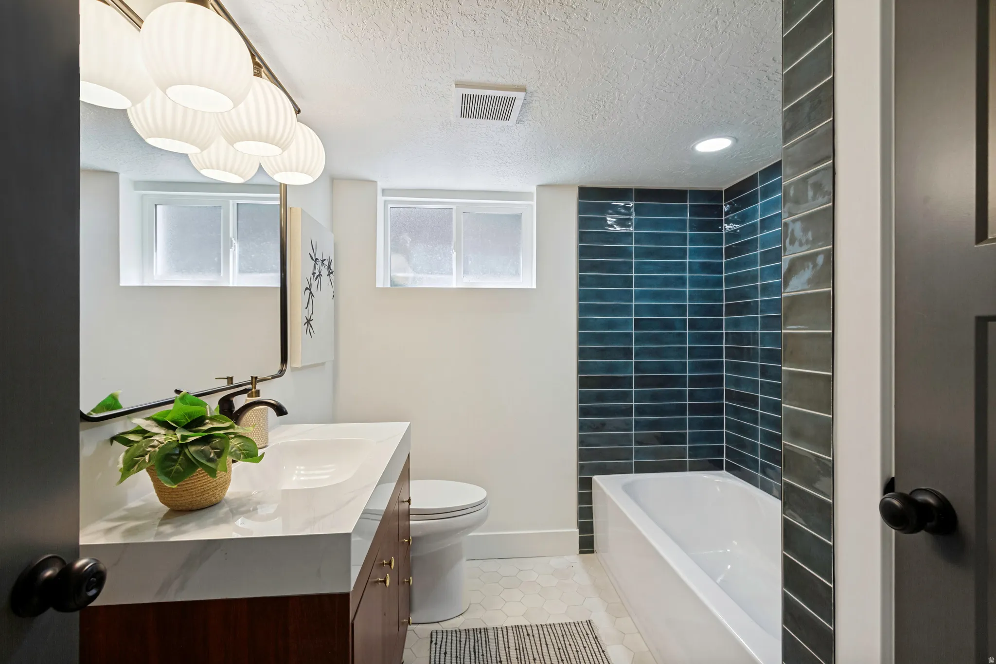 Sleek vanity with a rectangular undermount sink, a subway-tiled shower with tub, and hexagonal floor tiling