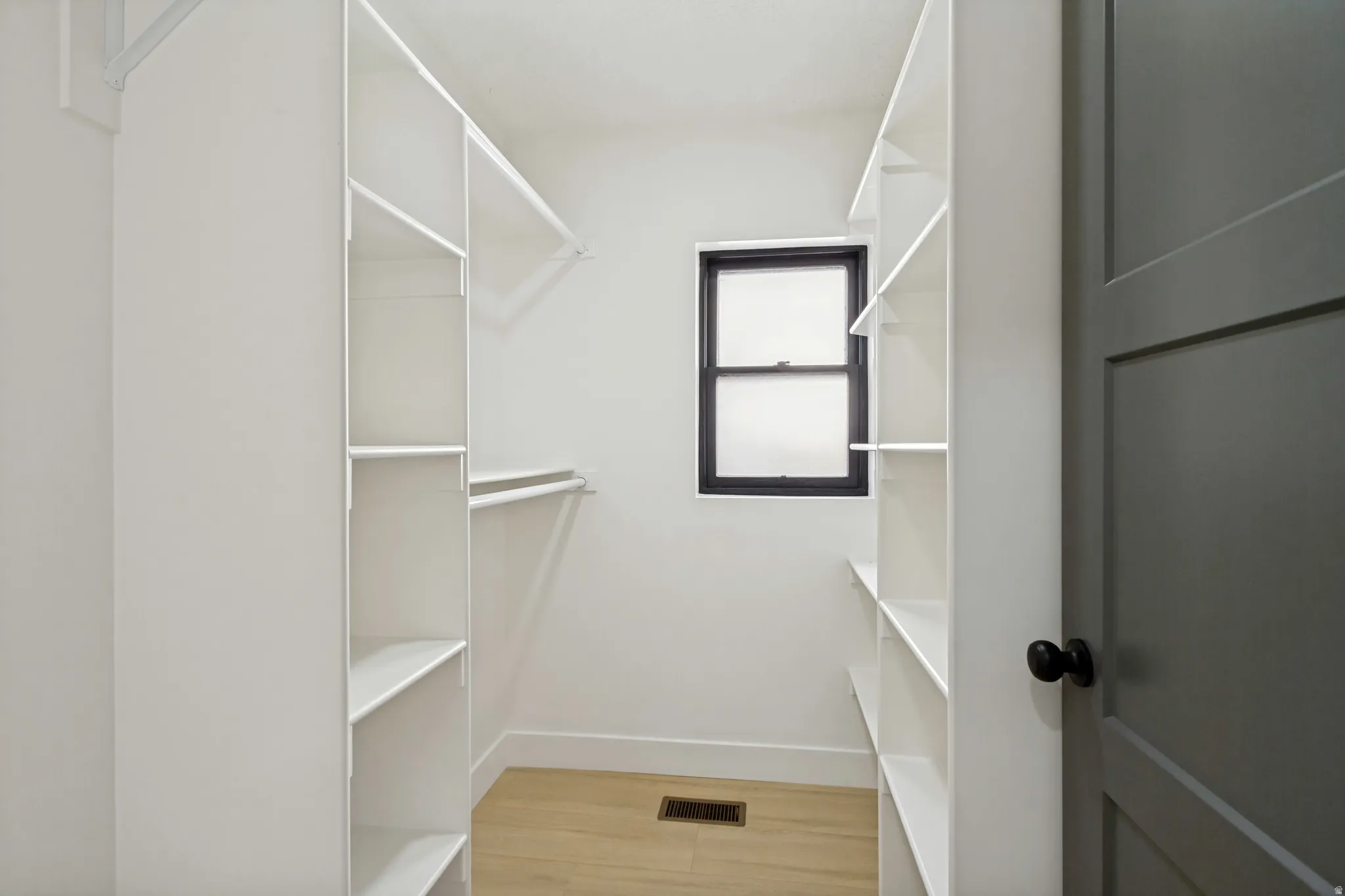 Walk-in closet featuring built-in shelving, hanging rods, and a window with a dark frame