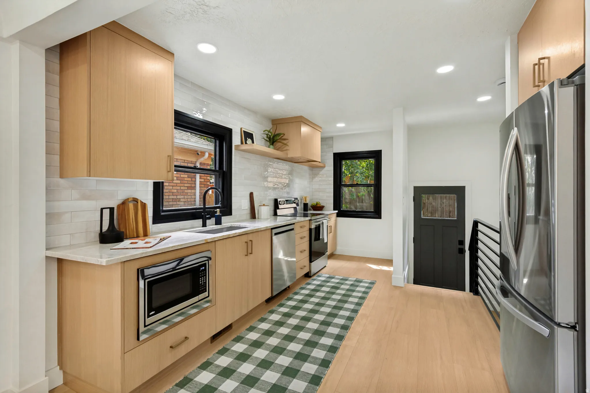 Kitchen featuring light wood cabinetry, light-toned countertops, a tile backsplash, stainless steel appliances, and wood-finish flooring