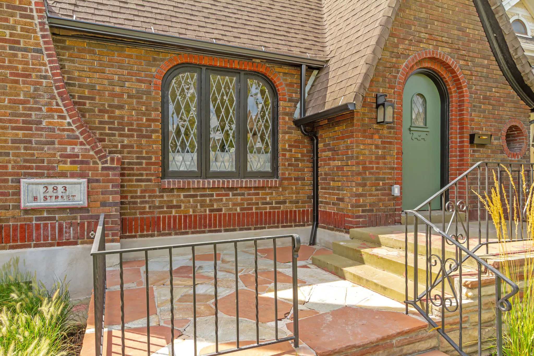 Brick exterior with an arched entry door, leaded glass window, stone steps, and wrought iron railings