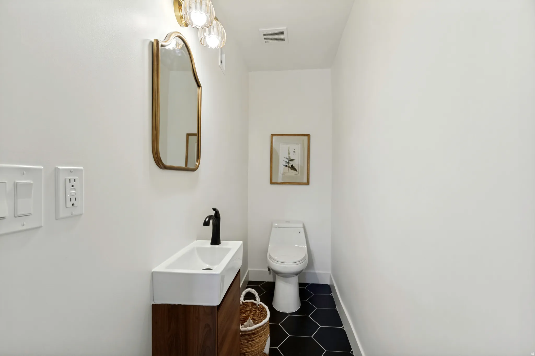 Powder room featuring a wood-finish vanity with an integrated rectangular sink, matte black faucet, and a gold-framed mirror