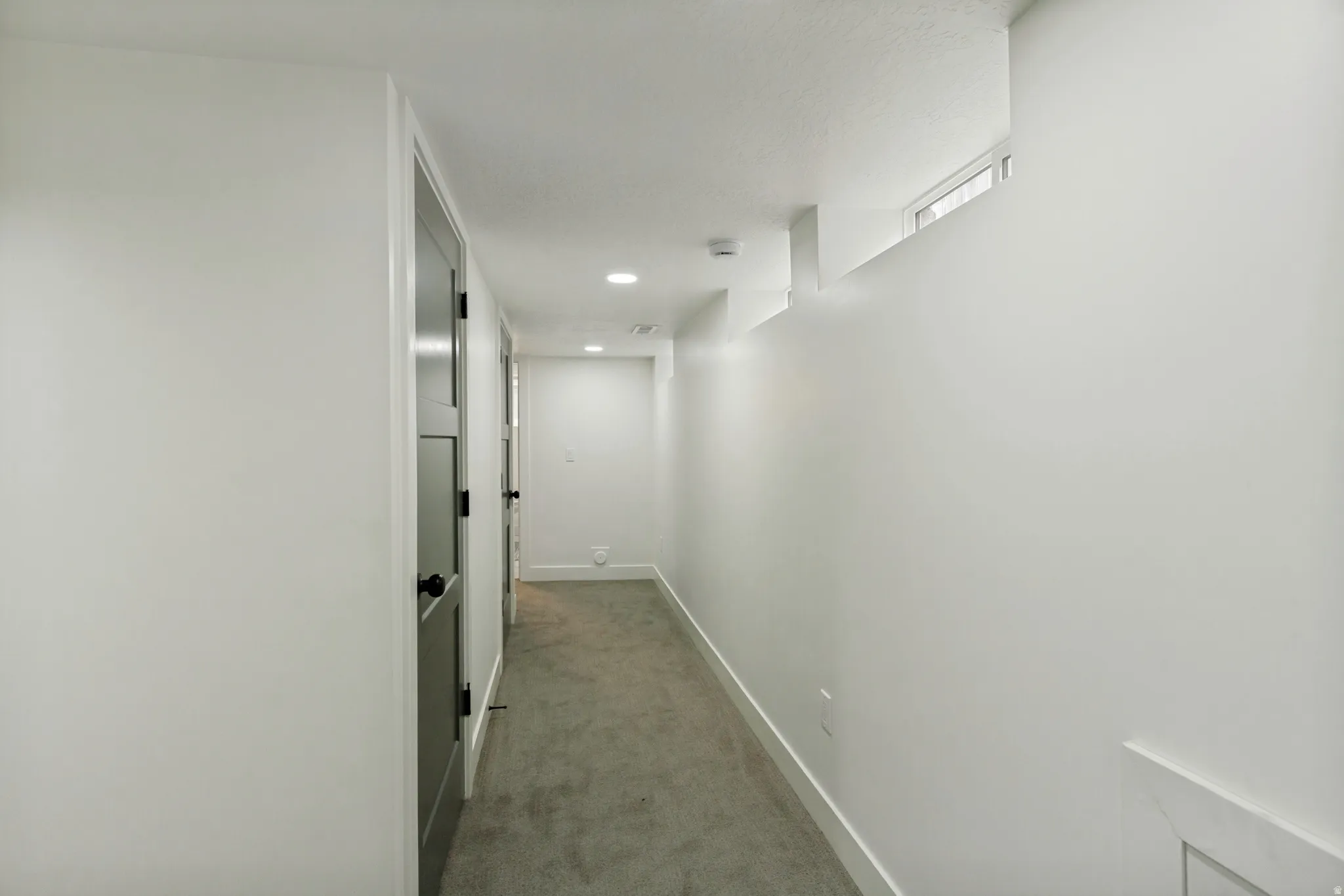 Hallway featuring light gray carpeting, recessed lighting, and modern panel doors with black hardware