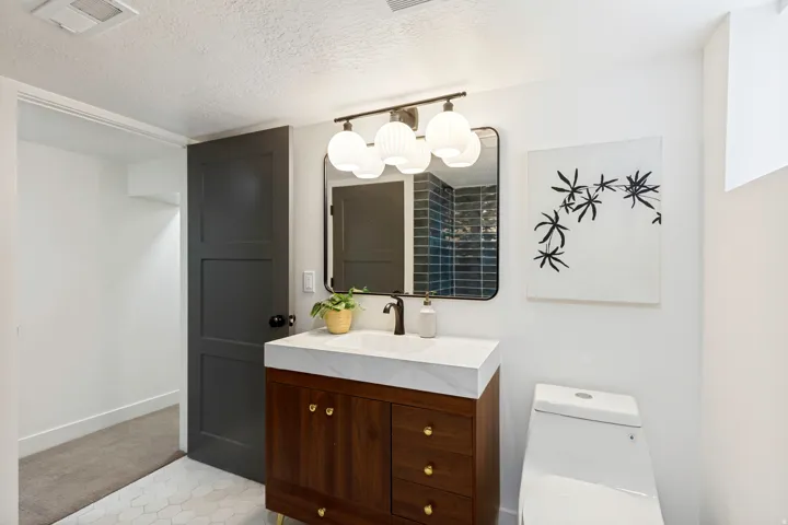 Hexagonal tile flooring, wood-finish vanity with gold-tone hardware, rectangular undermount sink with matte black faucet, contemporary mirror, and spherical vanity lighting