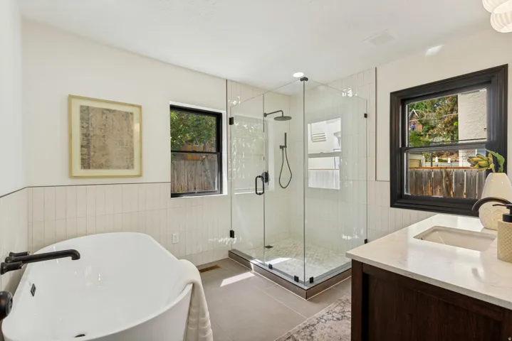 Freestanding soaking tub with dark bronze fixtures, glass-enclosed shower with subway tile surround, dark wood-finish vanity with an integrated sink, and white countertops