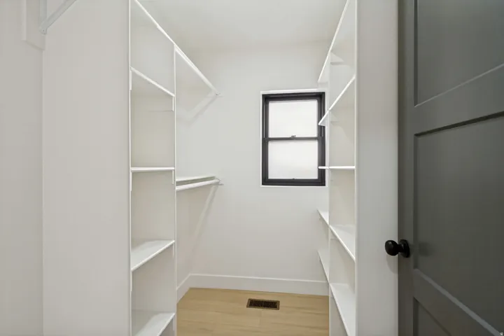 Walk-in closet featuring built-in shelving, hanging rods, and a window with a dark frame