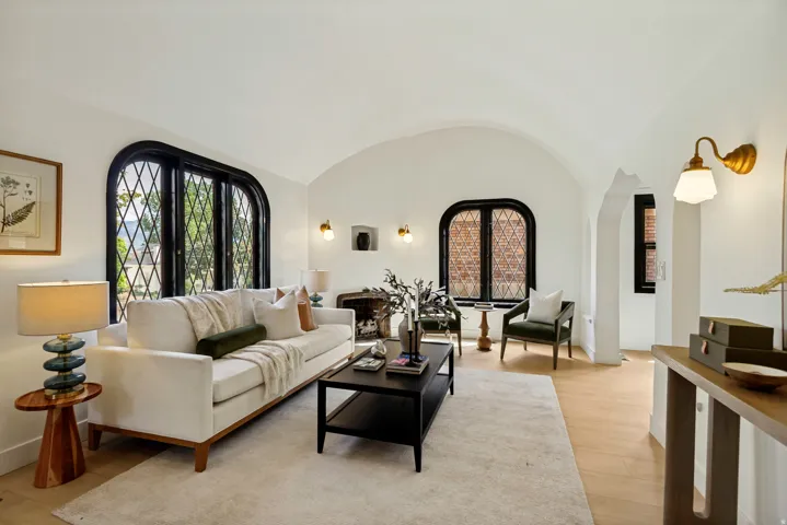 Vaulted ceiling with arched doorways, unique arched windows with black frames, wood-finish flooring, and wall-mounted sconces