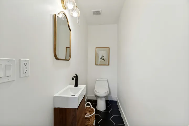 Powder room featuring a wood-finish vanity with an integrated rectangular sink, matte black faucet, and a gold-framed mirror