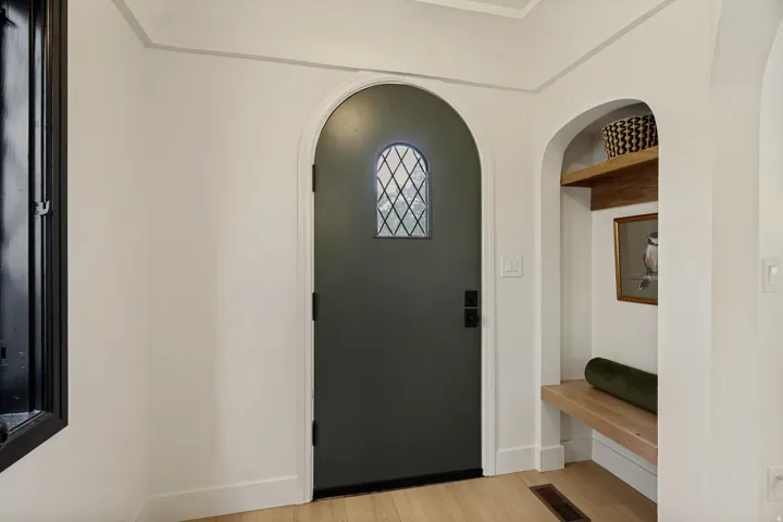 Arched entry door with leaded glass insert, wood-finish flooring, and built-in arched niche with wood shelving and bench