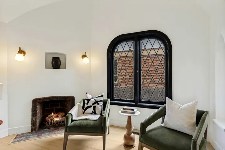 Arched window with diamond-patterned muntins, rustic fireplace with tile hearth, built-in wall niche, and light wood-finish flooring