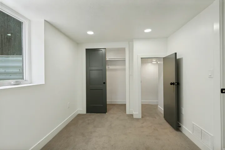 Recessed lighting, neutral carpeting, white walls, dark paneled doors, and a window with a window well