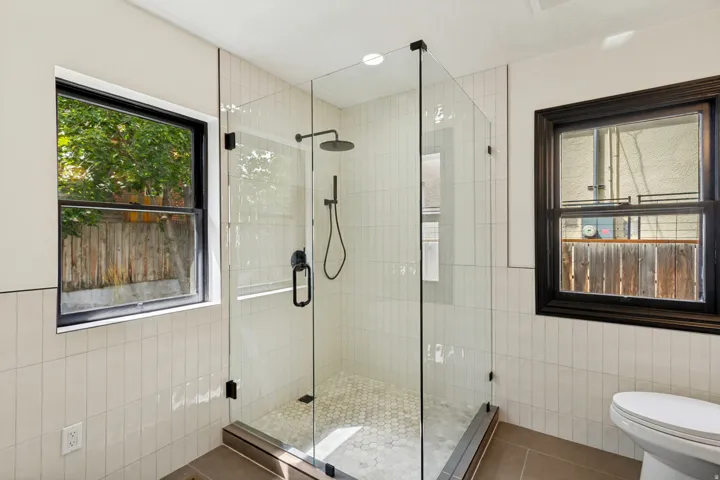Glass-enclosed shower with a rain showerhead, hexagonal floor tiling, and matte black fixtures