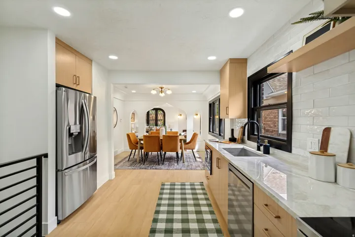 Stainless steel French door refrigerator, wood-finish cabinetry, light-toned countertops, white subway tile backsplash, and a black-framed window