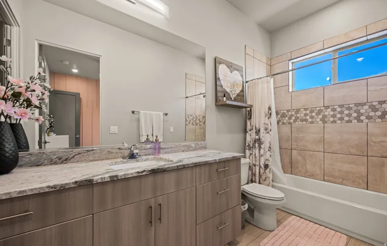 Bathroom featuring a single vanity with a stone countertop, a built-in tub with a shower, and light-toned wall tiling