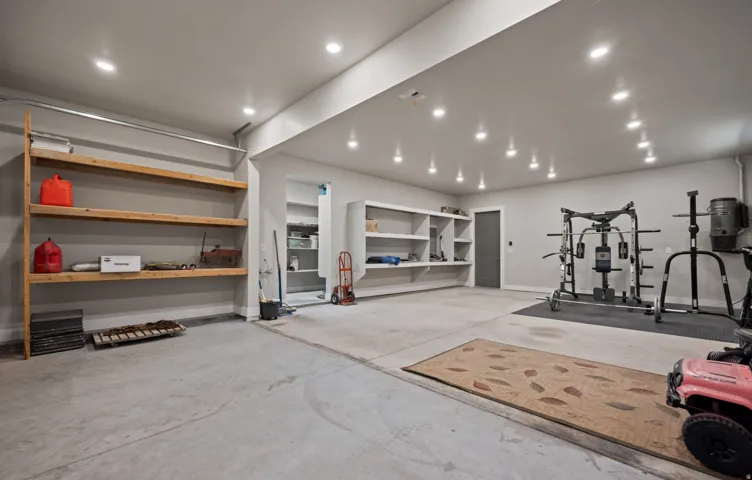 Spacious utility area featuring concrete flooring, built-in shelving, recessed ceiling lighting, and a solid panel door