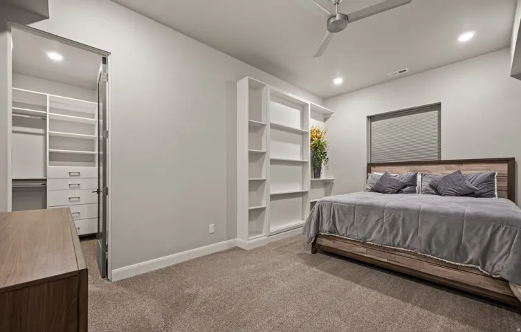 Recessed lighting, ceiling fan, built-in shelving, organized closet system with drawers, and carpeted flooring. HIDDEN VAULT BEHIND BOOKSHELF