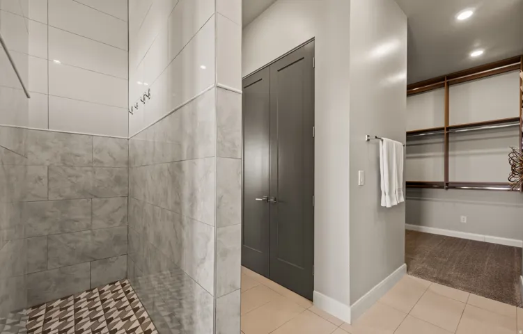 Primary Bathroom Suite Featuring Walk-In Shower with Geometric Tile Flooring, Large-Format Ceramic Wall Tile, Recessed Lighting, and Adjoining Walk-In Closet with Shelving and Rod Storage