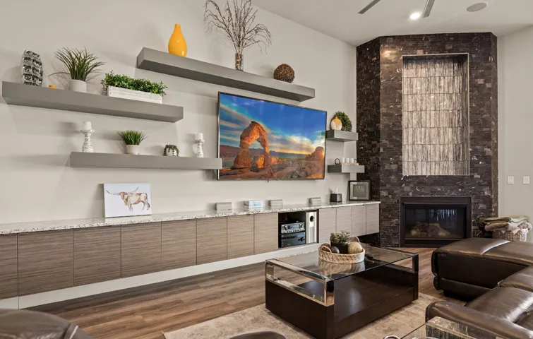 Built-in entertainment center with a light-colored countertop and wood-finish cabinetry, floating shelves, wood-finish flooring, and a fireplace with a textured stone surround