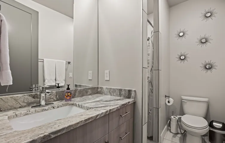 Vanity with integrated sink and stone countertop, wood-finish cabinetry, chrome faucet, and a wall-mounted mirror