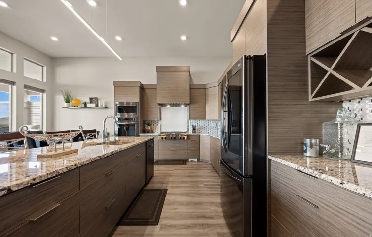 Kitchen featuring a large central island with a granite countertop and undermount sink, wood-finish cabinetry, stainless steel appliances, and wood-finish flooring