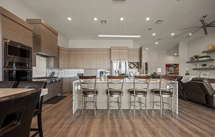 Gourmet MAIN KITCHEN with stainless steel appliances, built-in double ovens, a gas range, and a spacious island featuring stone countertops and a decorative tile facade