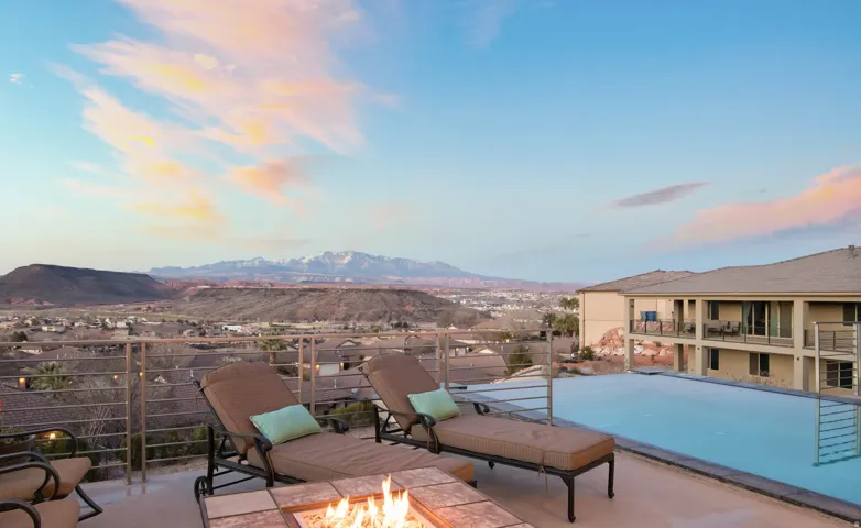 Infinity-edge pool with mountain backdrop, expansive patio, and built-in fire pit