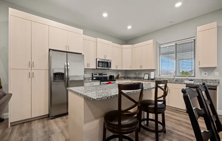 Kitchen featuring light wood-finish cabinetry, stainless steel appliances, speckled stone countertops, and wood-finish flooring