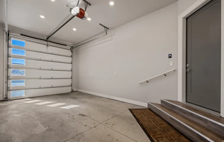 Concrete flooring, overhead garage door with multiple window panels, recessed ceiling lighting, wood-finish stair treads with metal nosing, and a contemporary interior door