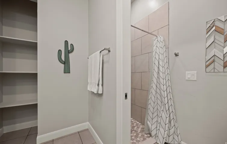 Built-in shelving for storage, tiled flooring, and a shower with full-height tile surround and hexagonal floor tiles