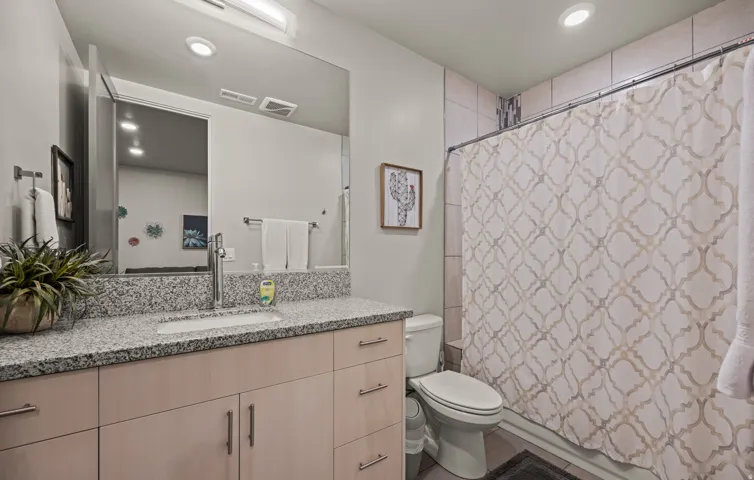 Spa-inspired bathroom featuring a floating vanity with ample storage, speckled stone countertop, and large framed mirror with integrated lighting