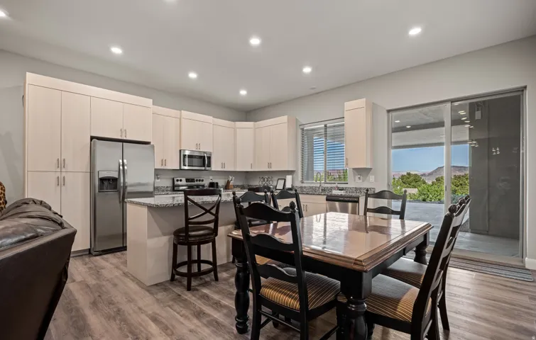 Open-concept BASEMENT APARTMENT KITCHEN and dining area featuring white cabinetry with stainless steel appliances, wood-finish flooring, a large center island with seating, and expansive glass sliding doors opening to an outdoor patio with water views