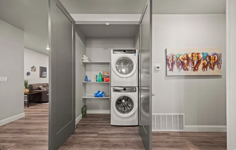 Dedicated laundry alcove with stacked appliances and built-in shelving, complemented by wood-finish flooring