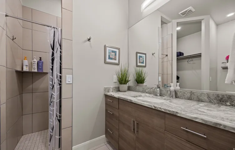 Recessed lighting, wood-finish vanity with chrome hardware, integrated rectangular sink, large vanity mirror, and a tiled shower with a built-in corner shelf