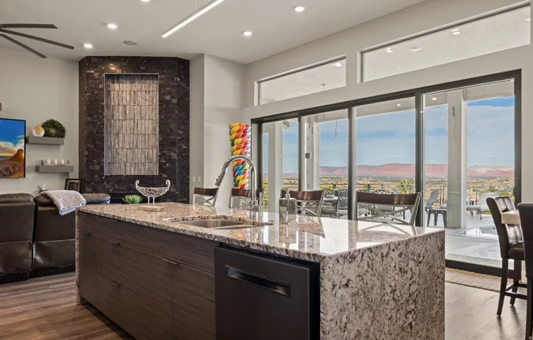Kitchen island with stone countertop and integrated sink, full-height sliding glass doors, transom windows, and a built-in water feature