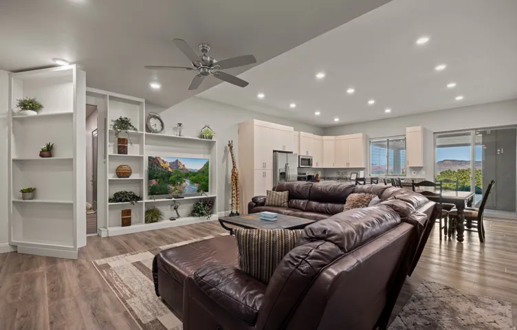 Open-concept living area with wood-finish flooring, built-in shelving, recessed lighting, and a ceiling fan