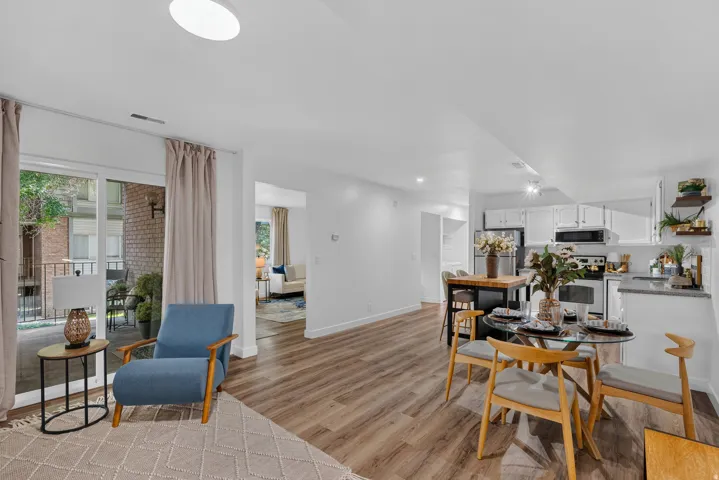 Open-concept living space featuring wood-finish flooring, a sliding glass door to an outdoor patio, and an integrated kitchen with white cabinetry and stone countertops