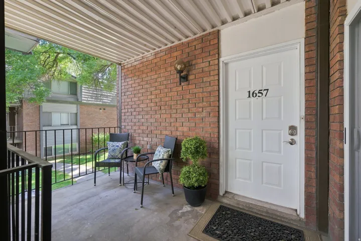 Covered patio with a brick exterior, metal railing, and a white entrance door