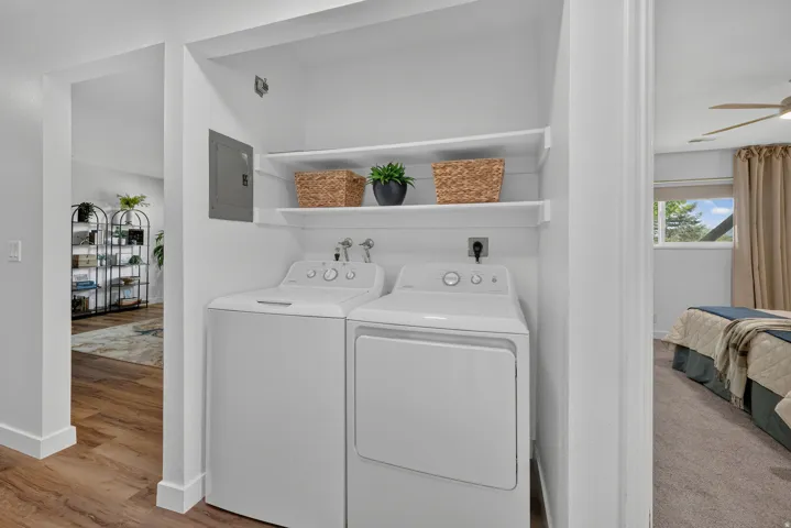 Dedicated laundry area featuring white appliances, integrated shelving, and wood-finish flooring