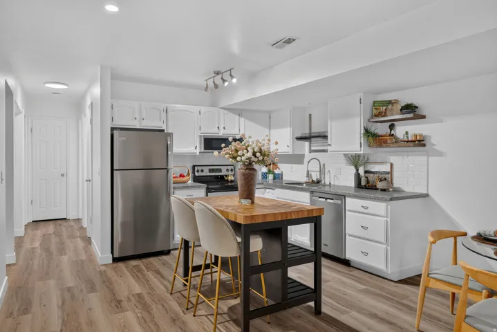 Modern kitchen featuring stainless steel appliances, white cabinetry with hardware accents, wood-finish countertops, and a center island with seating