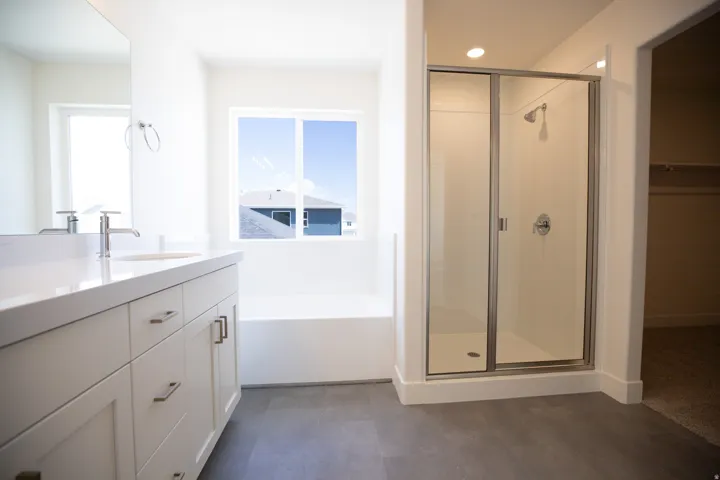 Primary bath with dual sinks, painted wood cabinets, quartz slab countertops, soaker tub and walk-in shower.