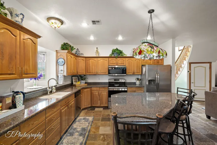 Kitchen featuring wood cabinetry, stainless steel appliances, a multi-level island, and stone tile flooring