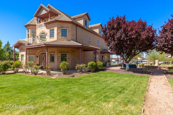 Stucco and stone exterior with multiple dormer windows, a covered front porch, and an upper-level balcony
