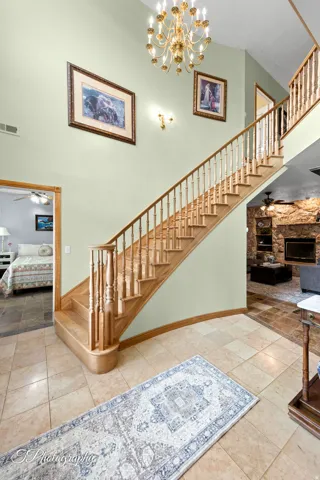 Two-story foyer featuring a grand staircase with wood banisters, tile flooring, and a decorative chandelier